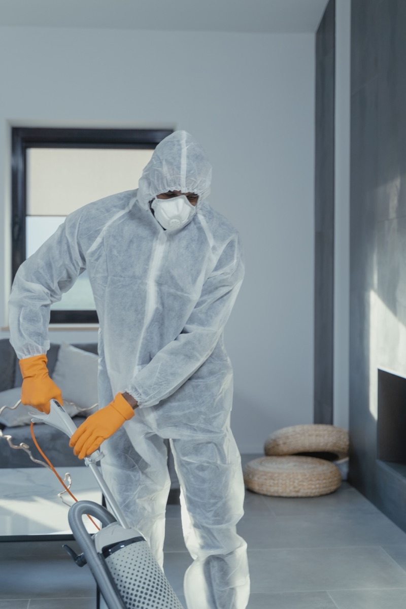 Cleaner in protective coveralls deep cleaning a living space