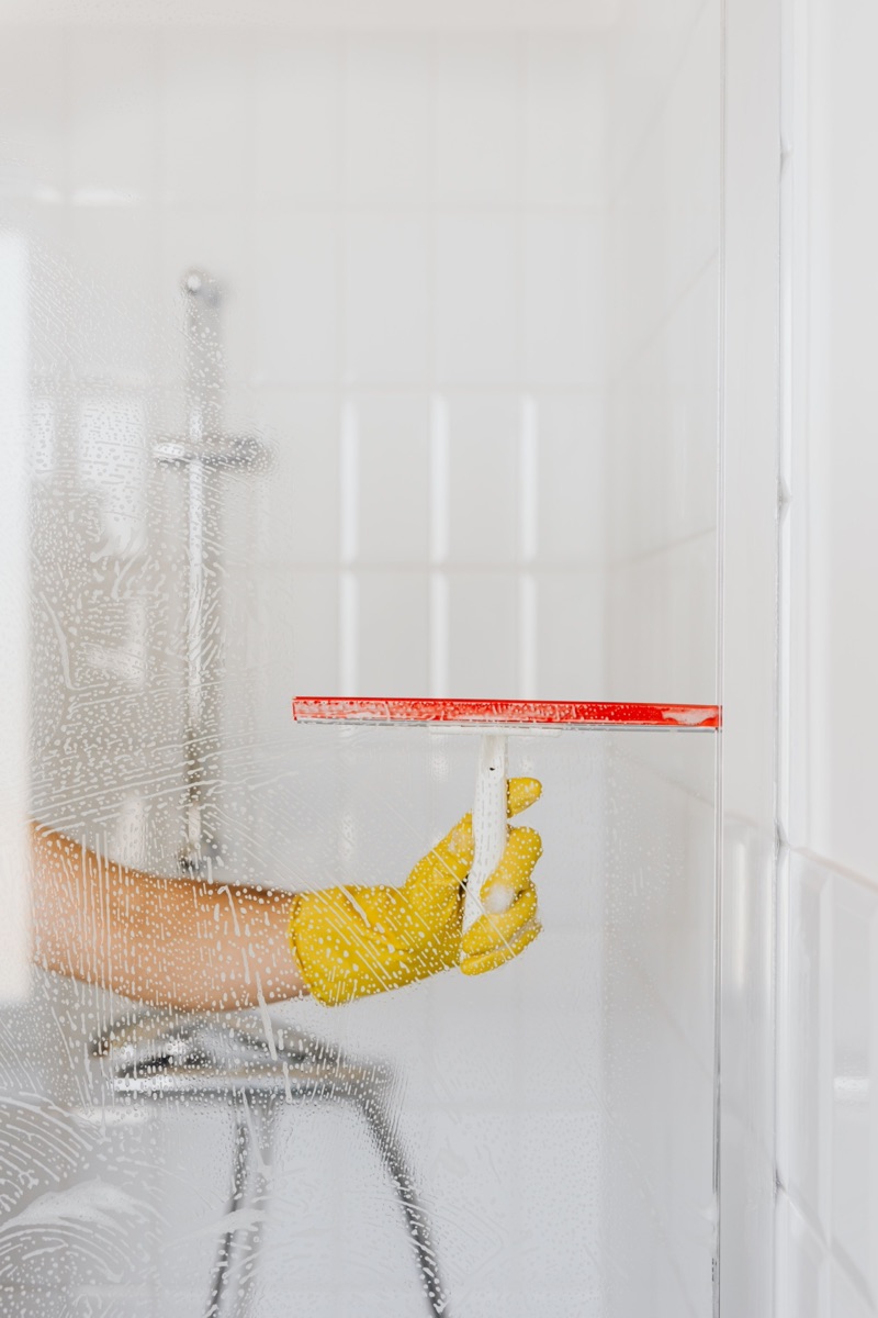 Gloved hand squeegeeing a shower screen for an end of tenancy clean