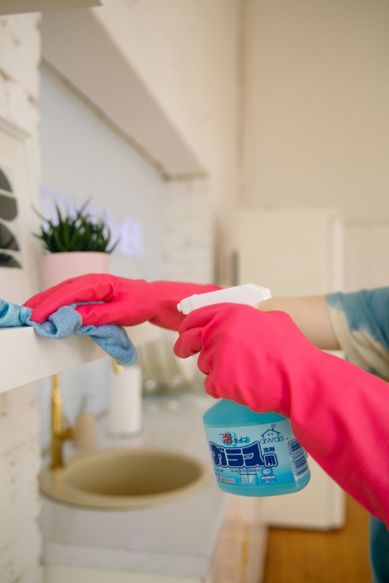Gloved hands wiping down a kitchen shelf during a house clean